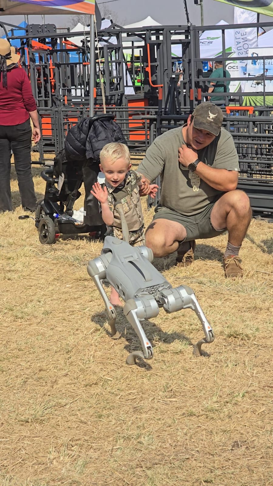 A small child reaching out toward the Unitree Go2 robot as it walks on the MCM Robotics stand