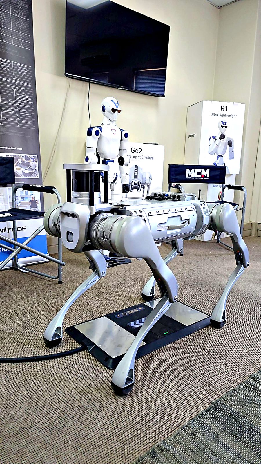 Side view of the Unitree B2 quadruped standing above the B2 contact charger board in the MCM Midrand showroom