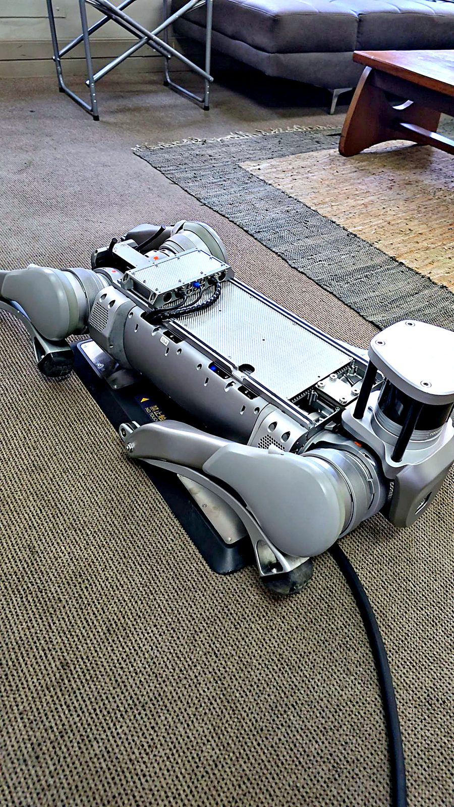 Unitree B2 quadruped robot lying on its contact charging plate, with the LiDAR at the front