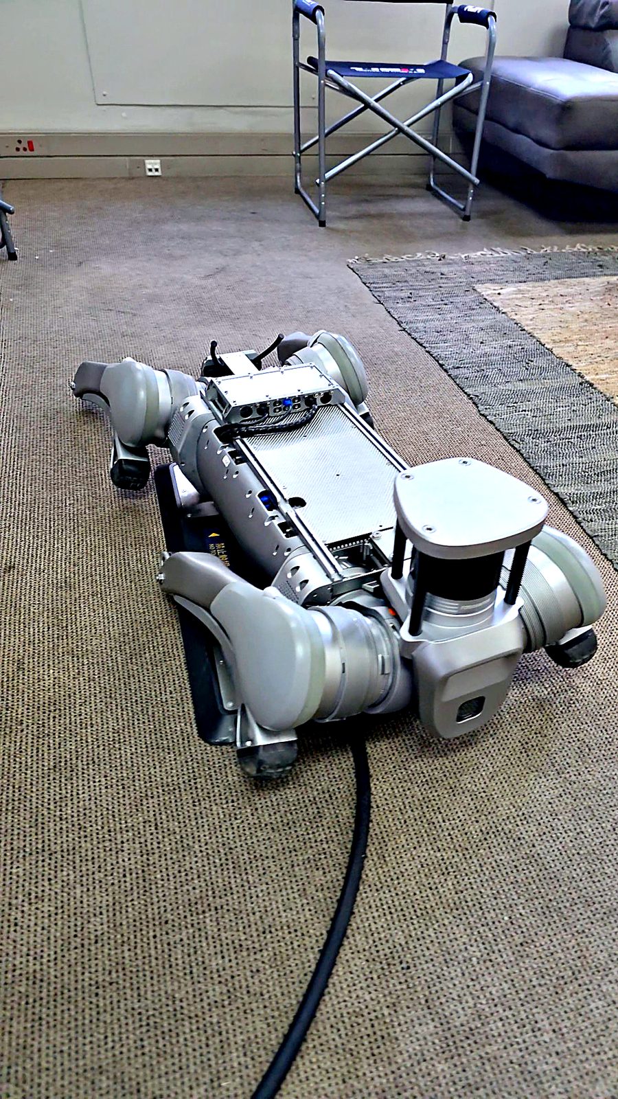 Rear view of the Unitree B2 lying down on the charging station so its abdomen electrodes touch the plate